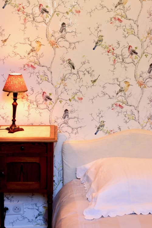 Elegant bedroom at Domaine de Bort with ornate wallpaper, wooden nightstand, red lamp, and white bedding overlooking the