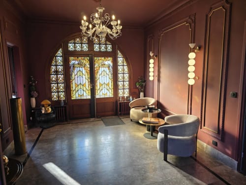Élégant hall d'entrée du Castel Bayeux aux murs en terre cuite, portes vitrail, lustre en cristal et mobilier contemporain