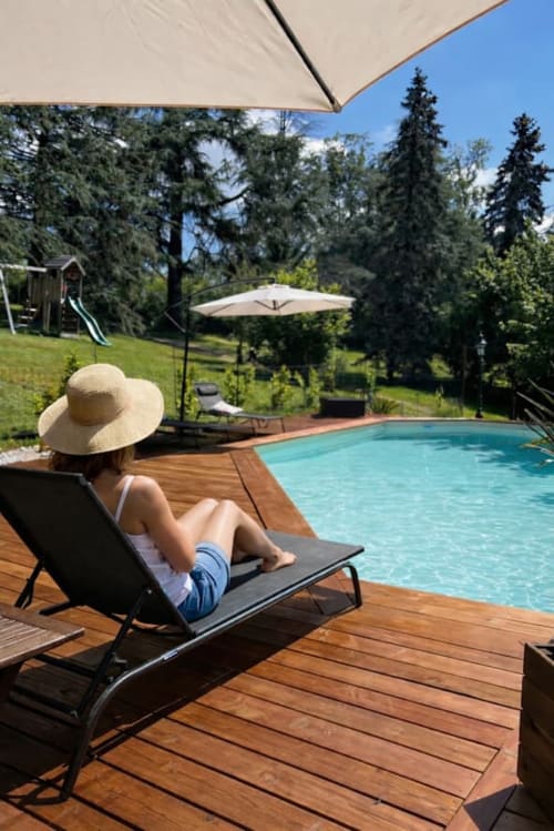 Femme relaxant dans un transat au bord de la piscine du Domaine le Manoir à Fossemagne, avec vue sur la forêt et parasol