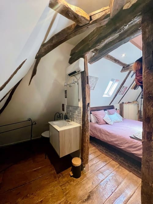 Chambre mansardée rustique avec poutres apparentes, literie rose, lavabo moderne et puits de lumière au gîte Domaine le Manoir