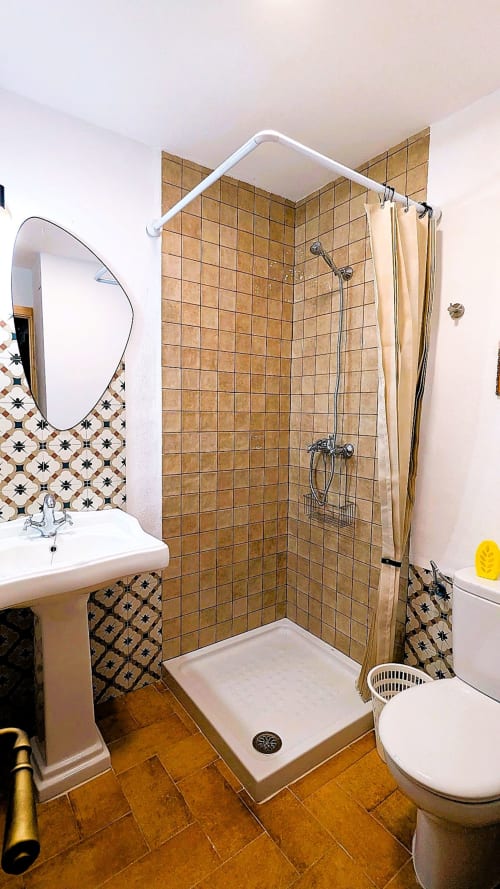 Cuarto de baño moderno con ducha de azulejos marrones, lavamanos de pedestal y piso con patrón geométrico en la villa Casa Rural Ribera del Huéznar