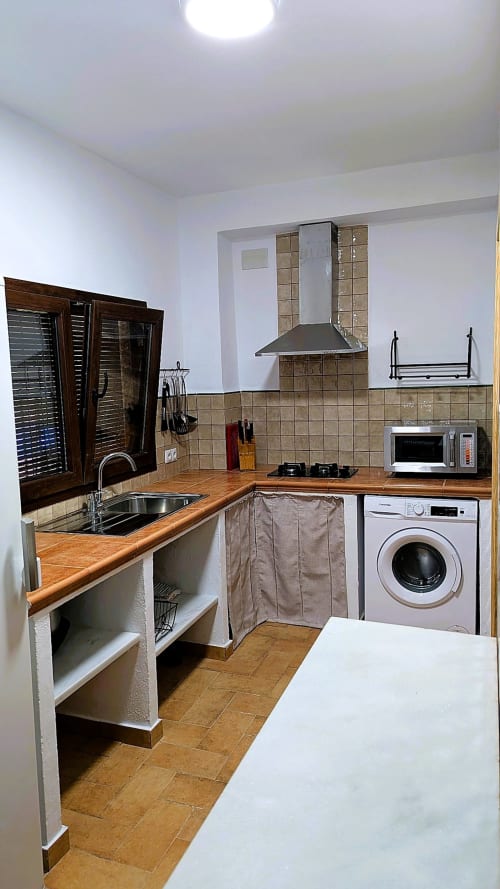 Cocina moderna con encimeras de madera, salpicadero de azulejos, lavadora y microondas en Casa Rural Ribera del Hueznar,