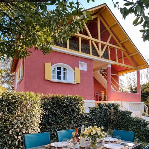 Le gîte La Maison Joséphine en Dordogne : façade rouge, pignon bois, terrasse repas et haie de lierre
