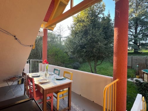 Terrasse couverte avec chaises colorées offrant une vue sur les jardins verdoyants du gîte Domaine le Manoir en Dordogne