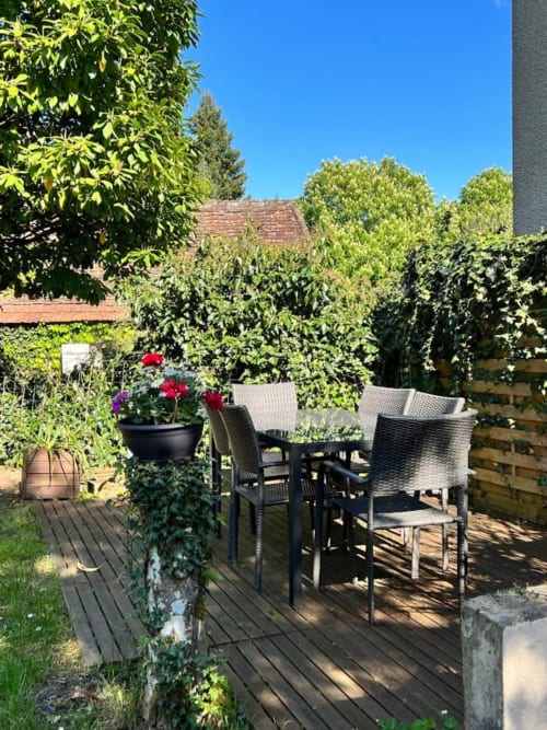 Terrasse ensoleillée du gîte Domaine le Manoir en Dordogne avec ensemble de repas, plantes fleuries et verdure luxuriante