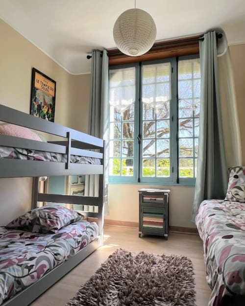 Chambre d'enfants lumineuse au Domaine le Manoir avec lits superposés, vue sur le jardin par de grandes fenêtres et literie florale