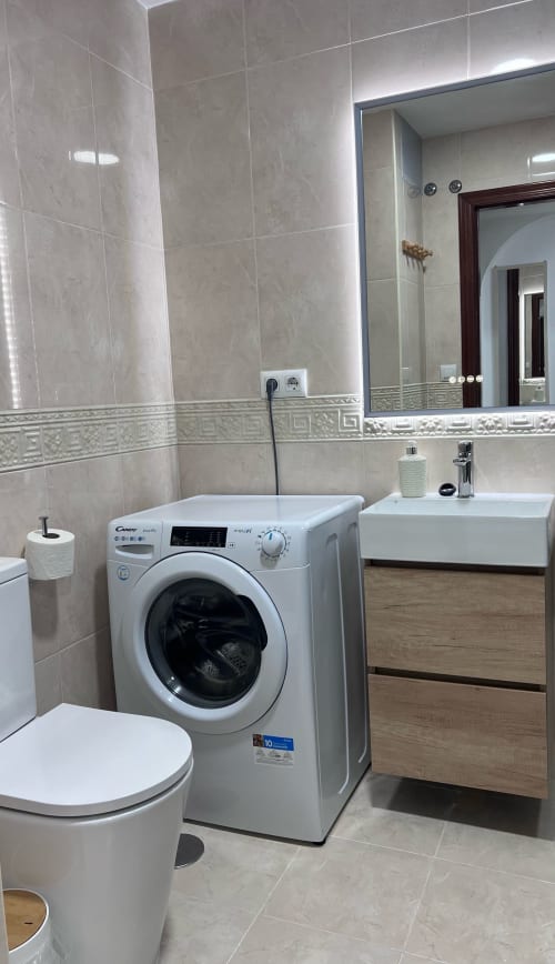 Modern bathroom at Brisa Marina apartment with washing machine, sink, toilet and beige tile walls