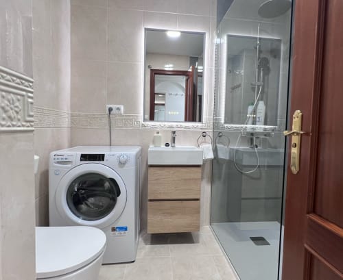 Modern bathroom in Brisa Marina apartment with washing machine, sink, mirror, and glass shower enclosure in Mazagon, Spain