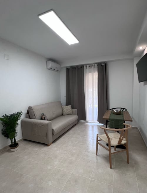 Modern living room in Brisa Marina apartment with beige sofa, wooden chair, sea-view balcony, and contemporary ceiling