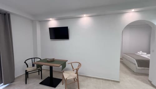 Modern living area in Brisa Marina apartment with dining table, chairs, wall-mounted TV, and bedroom visible through archway