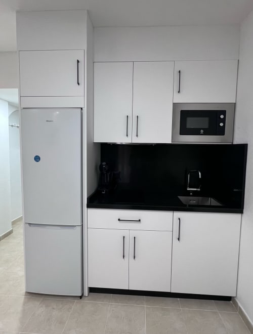 Modern white kitchen with black backsplash, microwave, and white refrigerator in Brisa Marina apartment, Mazagon