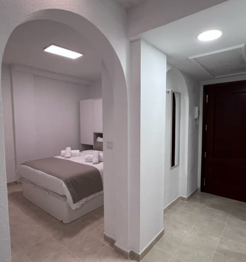Modern apartment bedroom at Brisa Marina Mazagon with arched alcove bed, white walls, LED lighting, and tiled flooring