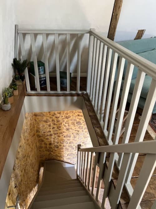 Chambre sous les toits chaleureuse au Domaine le Manoir avec balustrades blanches, poutres en bois et mur de pierre rustique à Fossemagne