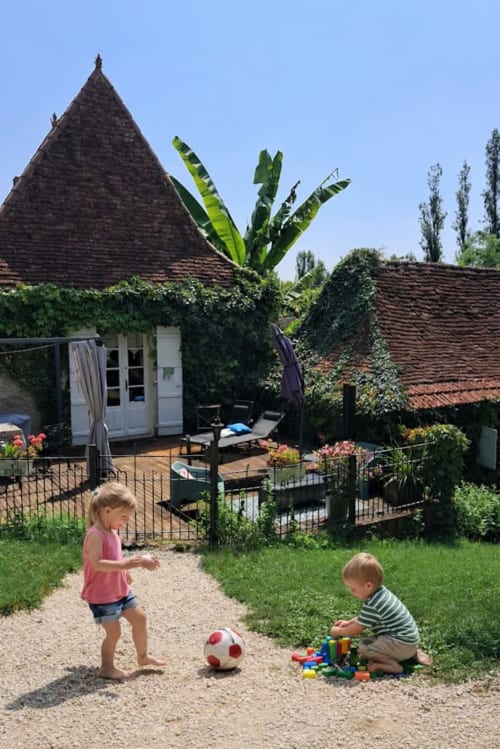 Jeunes enfants jouant dans le jardin du gîte Domaine le Manoir avec bâtiment aux toits coniques et murs couverts de lierre