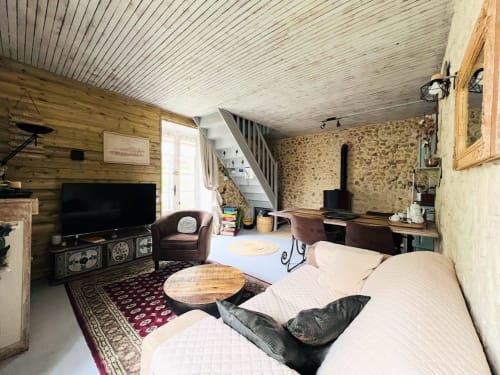 Intérieur rustique du Domaine le Manoir avec murs en bois, lit, télévision, cheminée en pierre et salle de jeux en Périgord Noir