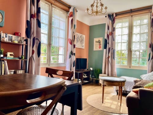 Chambre studio charmante au Domaine le Manoir aux murs orange et vert, mobilier en bois, rideaux à motifs et lumière naturelle