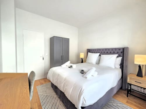 Chambre moderne dans un appartement de Levallois-Perret avec lit gris rembourré, linge blanc, tables de nuit en bois et ambiance