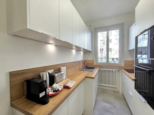 Cuisine contemporaine aux armoires blanches, plan de travail en bois et électroménagers intégrés dans un appartement à Levallois-Perret, près de Paris