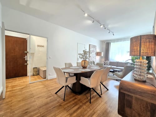 Salle à manger moderne à Levallois-Perret avec table ronde, chaises beiges, parquet et vue sur le séjour