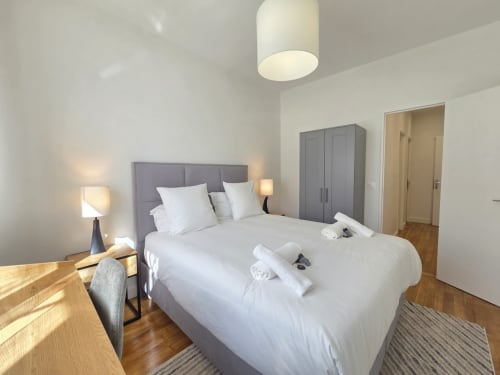 Chambre élégante avec lit capitonné gris, linge blanc, lampes de chevet, armoire et parquet à Paris.