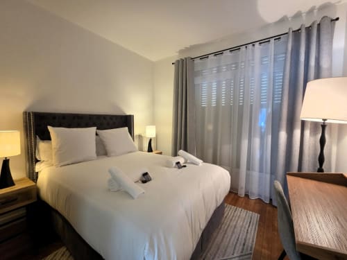 Chambre moderne avec literie blanche, tête de lit foncée, rideaux gris, parquet et luminaires contemporains à Paris