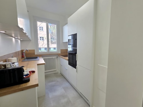 Cuisine galley moderne avec meubles blancs, plan de travail en bois et électroménagers noirs dans un appartement parisien près de La Défense