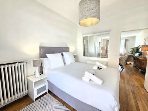 Chambre moderne à Levallois-Perret avec literie blanche, tête de lit grise, lampe suspendue et portes de placard miroir