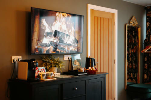 Boutique hotel room with fireplace TV display, black dresser, yellow door, and framed artwork at Shrewsbury's Baschurch House