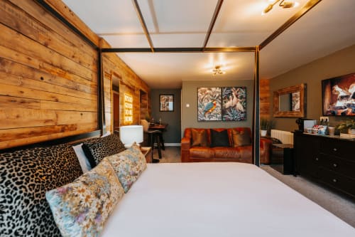 Luxe king bedroom with wooden canopy bed, leopard print pillows, orange leather sofa, and bird artwork at Shrewsbury boutique