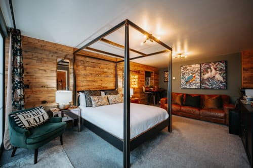 Luxurious king canopy bed in Cherry Tree Suite at Shrewsbury boutique hotel with wood paneling, leather sofa, and warm