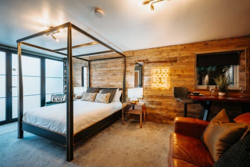 Luxurious king bedroom at Baschurch House Shrewsbury with four-poster bed, wooden walls, neon sign, and modern furnishings