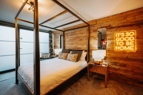 Luxurious king canopy bed in wood-paneled suite with neon 'It's So Good To Be Home' sign at Shrewsbury hotel