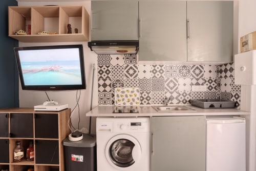Cuisine compacte avec crédence en carrelage motifs, lave-linge, placards blancs et TV à l'hôtel Queen And King, Chaville