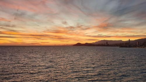 Puesta de sol sobre el Mar Mediterráneo con la costa de Benidorm y montañas recortadas contra un cielo dorado