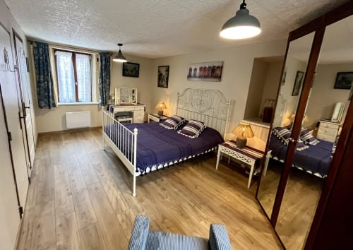 Chambre spacieuse au Gîte La Vieille Ferme de La Dounie avec lit en fer blanc, parure bleu foncé et vue sur le jardin