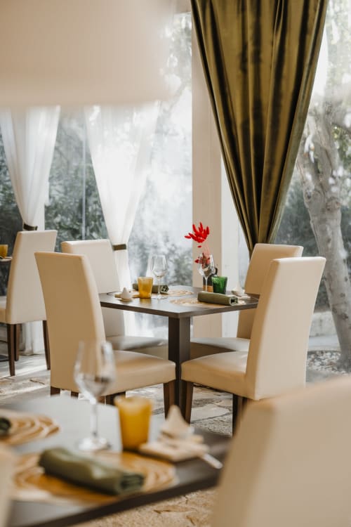 Elegante sala da pranzo di Villa Ceci B&B ad Andria con sedie color crema, tavolo scuro, fiori rossi e tende verde oliva