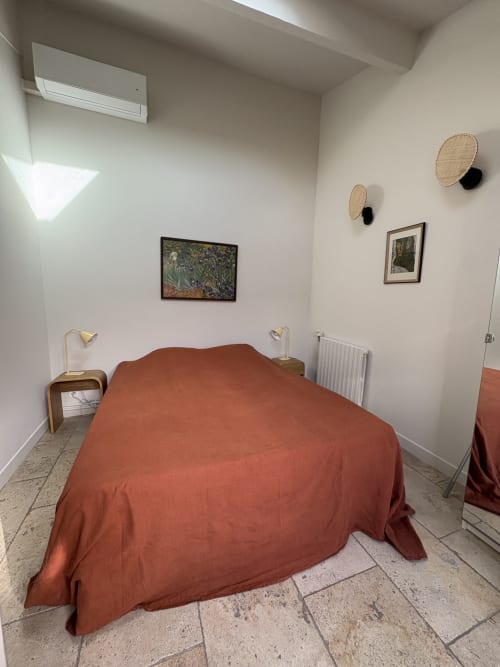 Chambre avec dessus-de-lit rouille, tables de nuit en bois, œuvres murales et lumière naturelle au Gîte château de Pannis à Arles.