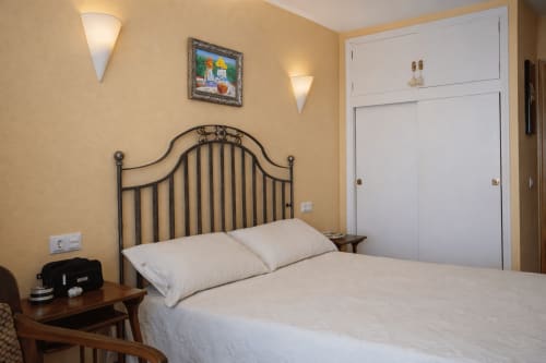 Dormitorio en Portofino Playa Apartamentos de Benidorm con cama de estructura metálica, almohadas blancas y paredes amarillas