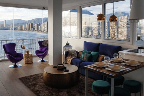 Apartamento de lujo en Benidorm con vistas al mar, sillas de terciopelo púrpura, sofá azul, lámparas colgantes de cobre, comedor y