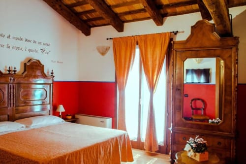Camera rustica in Agriturismo Villa Mocenigo con travi in legno, letti gemelli, parete rossa, tende arancioni e armadio
