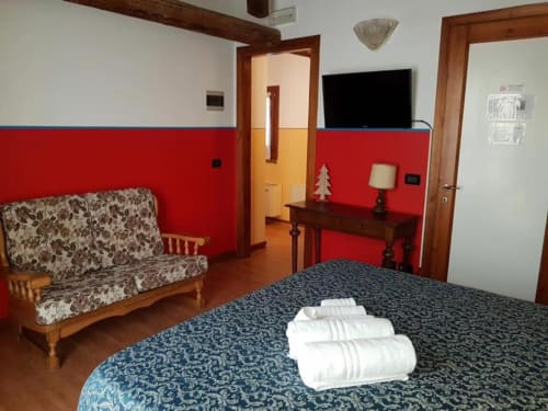 Camera tripla presso Agriturismo Villa Mocenigo con letto, asciugamani bianchi, divano, pareti rosse, travi in legno e TV a schermo piatto