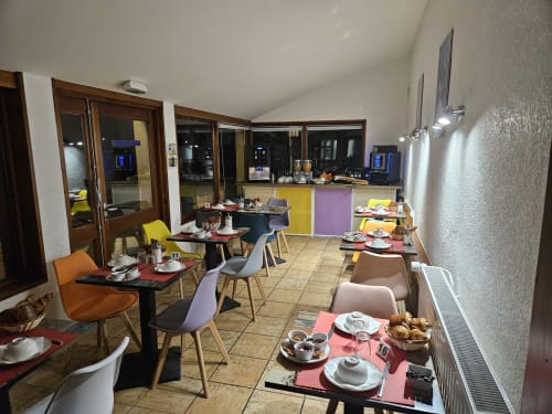 Salle de petit-déjeuner lumineuse à l'Auberge Du Campcardos à Porta avec chaises colorées, petites tables et pâtisseries
