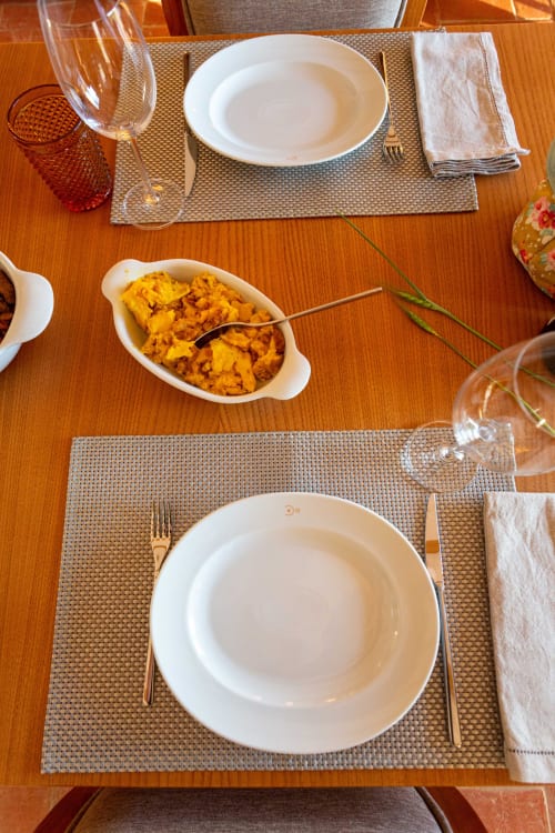 Mesa elegantemente arrumada na Pousada Cerro da Campaniça com pratos brancos, taças de vinho e prato de batata-doce