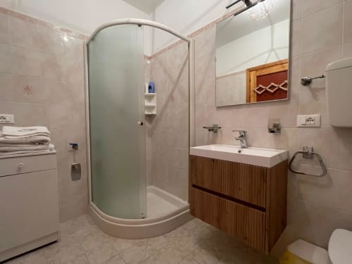 Moderno bagno nell'appartamento di Cesena con doccia in vetro curvo, mobile lavabo in legno e piastrelle rosa alle pareti
