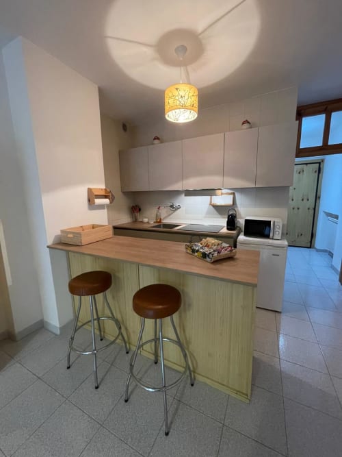 Cucina moderna con isola, sgabelli in legno e armadietti bianchi nell'appartamento Alba, Cesena