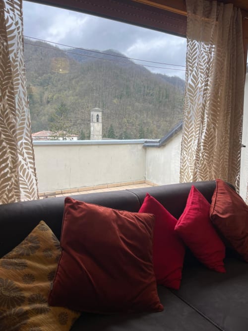 Divano nero con cuscini rossi sul balcone con vista montagna dell'appartamento LHE Alba a Cesena, Italia