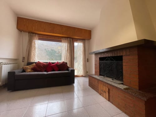 Soggiorno moderno con divano nero, cuscini rossi, camino e vista sulle montagne dal balcone dell'appartamento Alba a Cesena