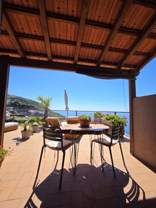 Terraço ensolarado de Les Terrasses Les Suites em Calheta com mesa de jantar, vistas para o mar e paisagem montanhosa