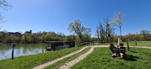 Saône-Tal-Lodges am Flussufer mit grüner Wiese, Kiesweg und vertautem Boot auf ruhigem Fluss bei Traves