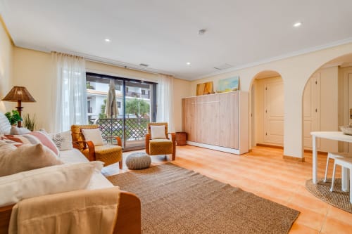 Espaçosa sala de estar acessível com azulejos de barro, sofá creme, poltronas laranja, sacada com vista para o jardim